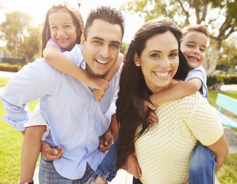 Parents Giving Children Piggyback Ride In Garden